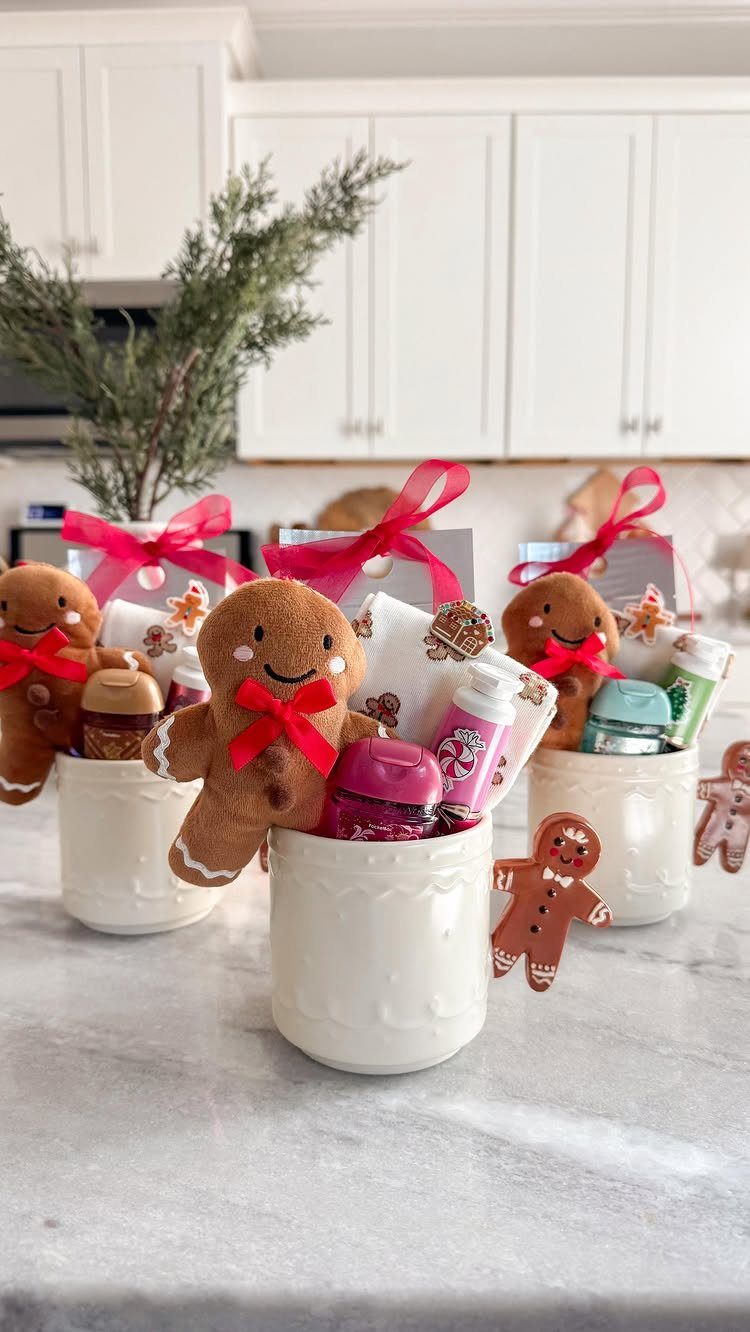 Three white mugs filled with gingerbread plushies and small gifts on marble countertop