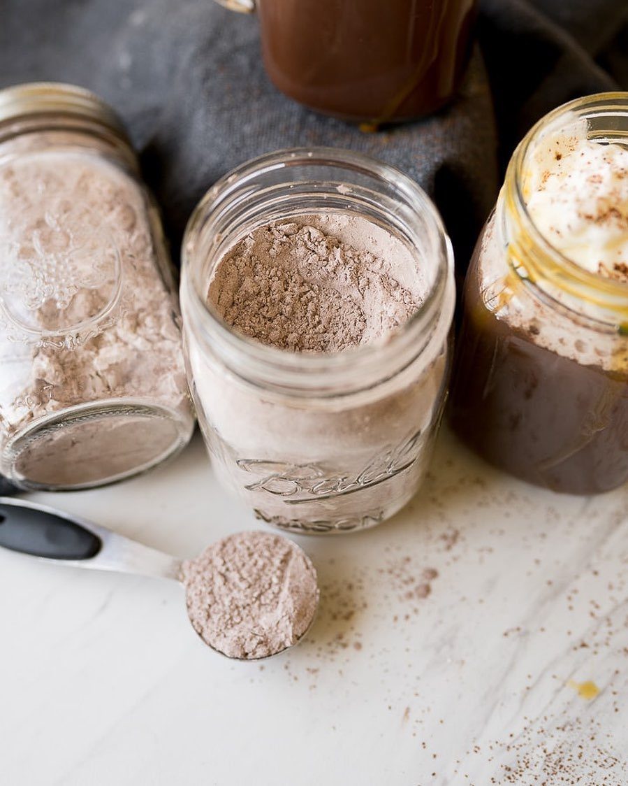 Hot chocolate mix in glass mason jars with a spoon of cocoa powder.