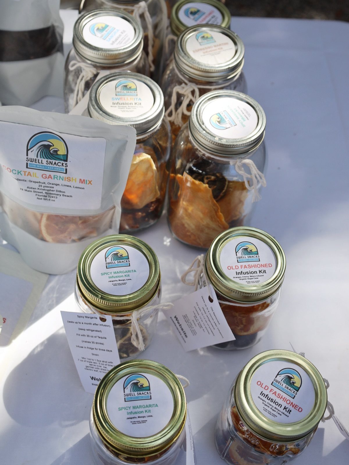 Glass jars containing dried fruit and spices for alcohol infusion kits on white table