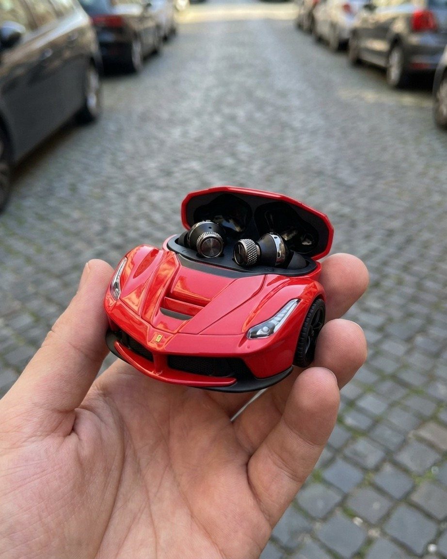 Red sports car shaped earbud case held in a hand on cobblestone street