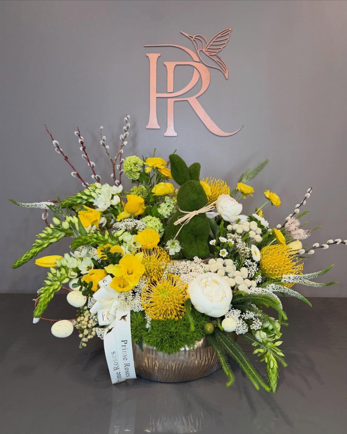 Floral arrangement with yellow and white flowers and a moss bunny in a bowl.