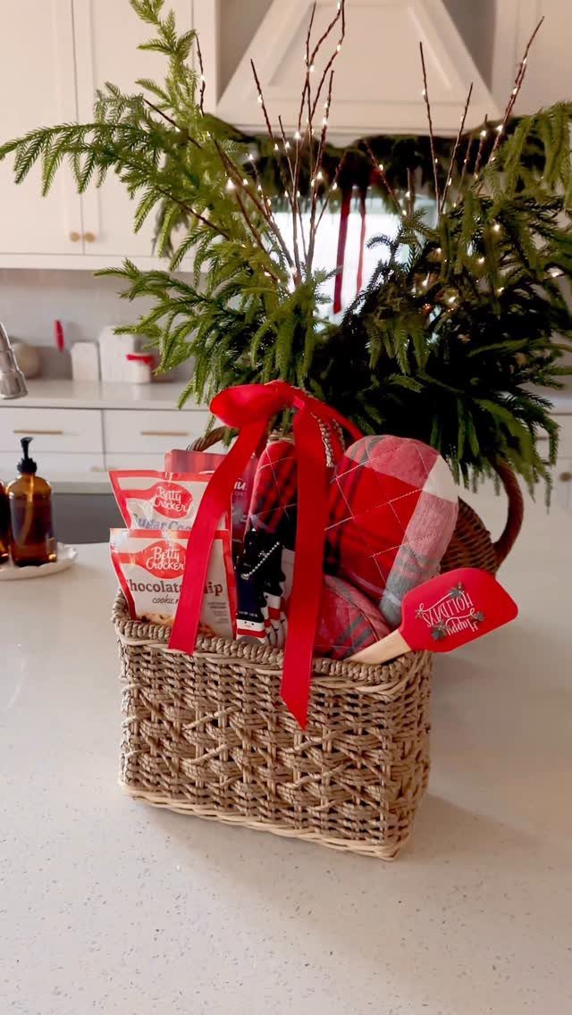 Woven gift basket with baking treats, red spatula, and red ribbon on kitchen counter