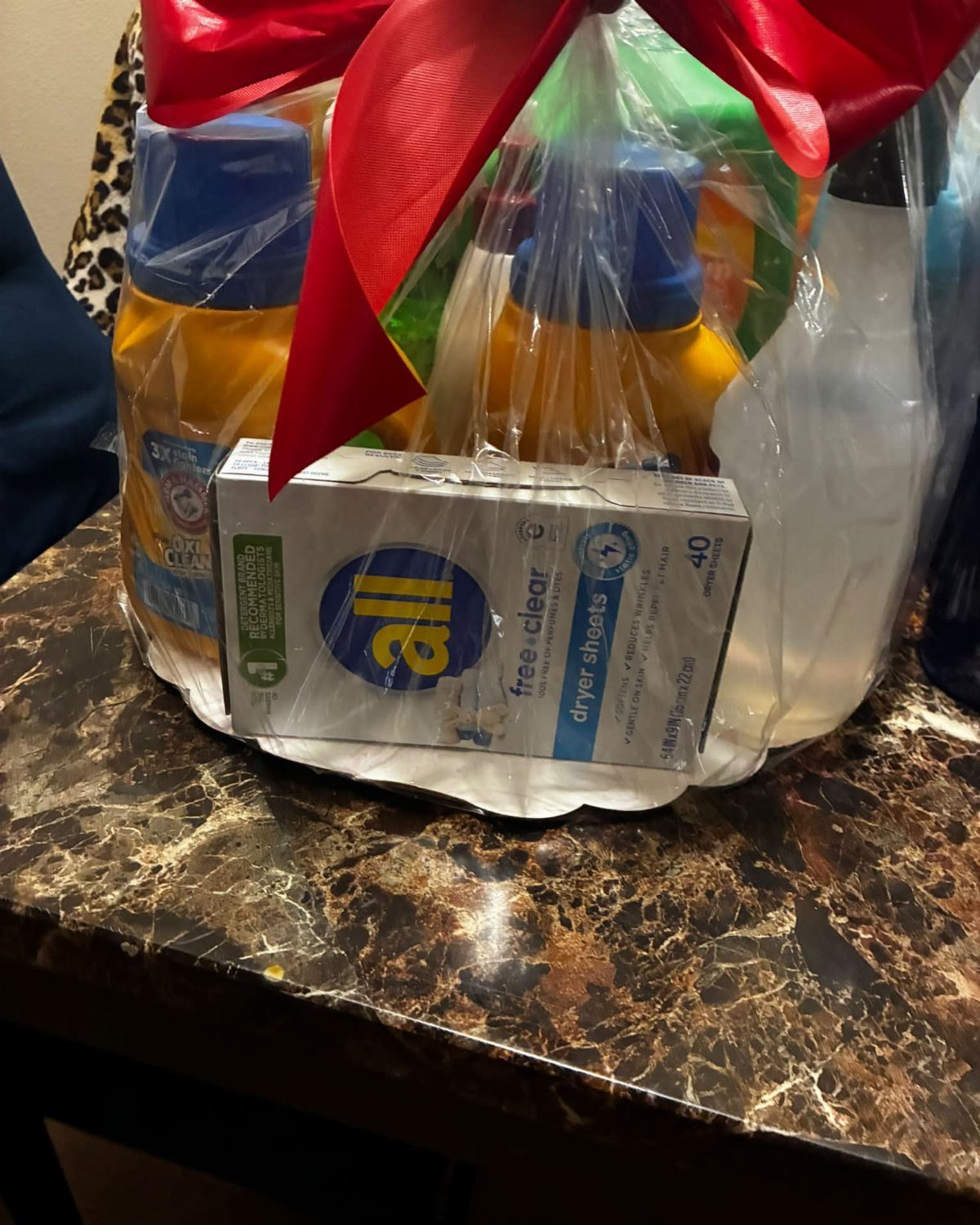 Laundry gift basket with detergent and dryer sheets wrapped in cellophane with red bow.