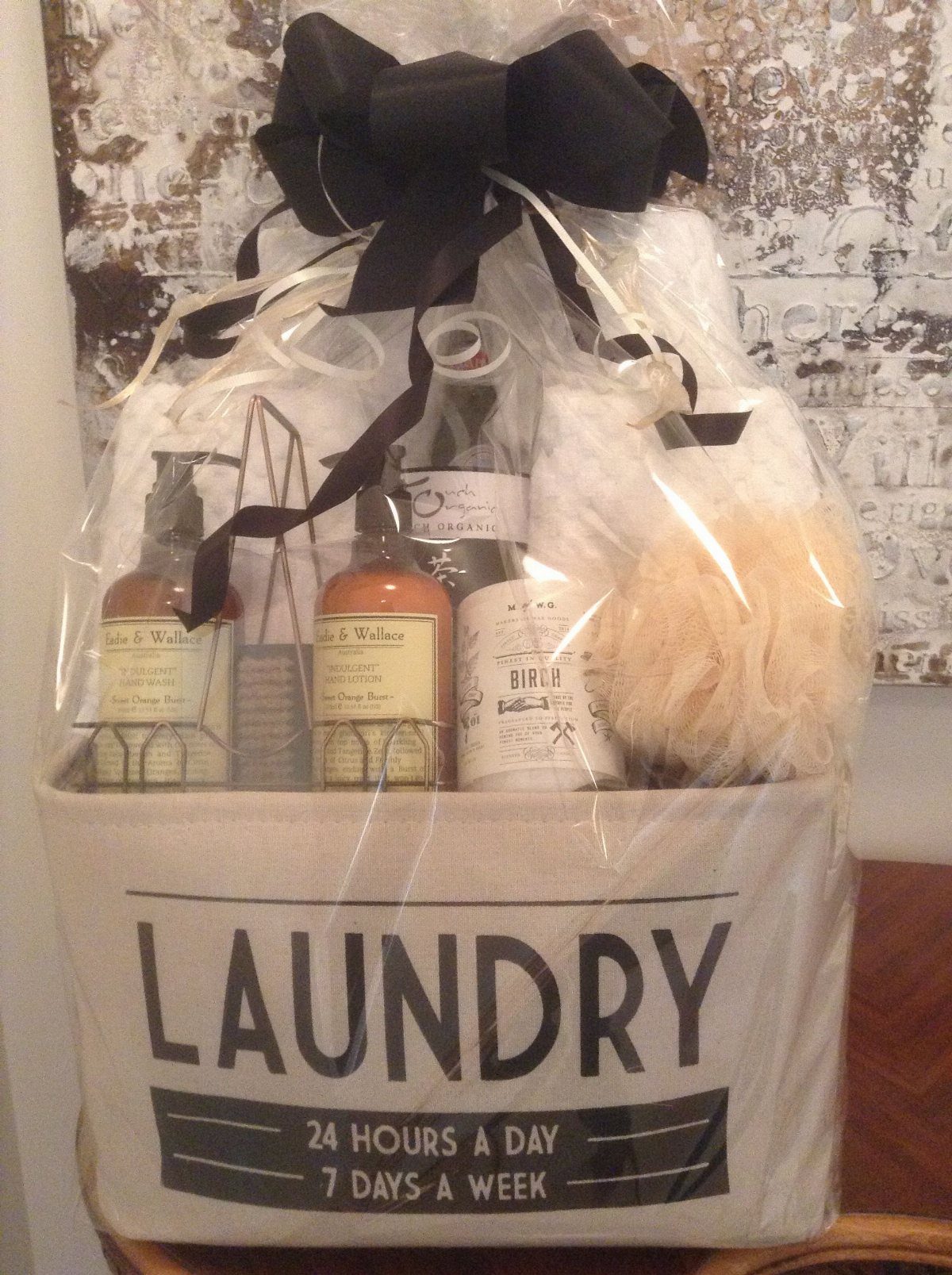 Laundry hamper gift basket wrapped in cellophane with a large black bow.