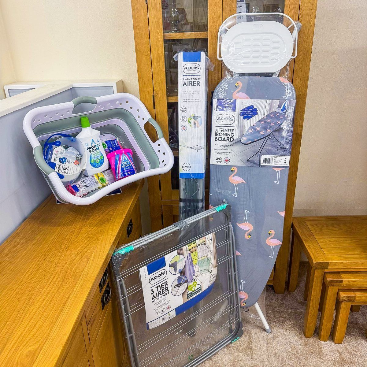 Laundry basket with detergents next to a flamingo ironing board and clothes airer.