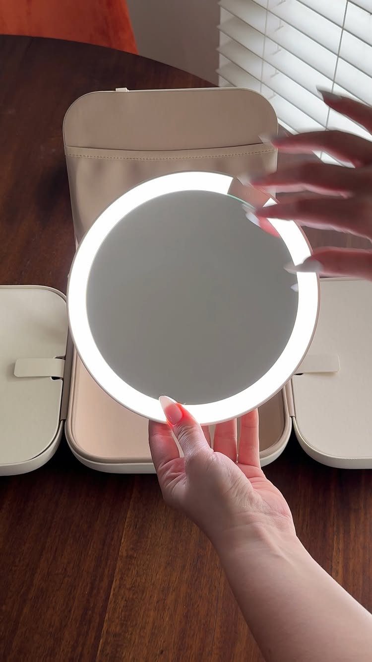 11 Mother in Law Birthday Gift Ideas She Will Actually Use 3 Circular LED makeup mirror held over an open beige fold-out makeup organizer bag.
