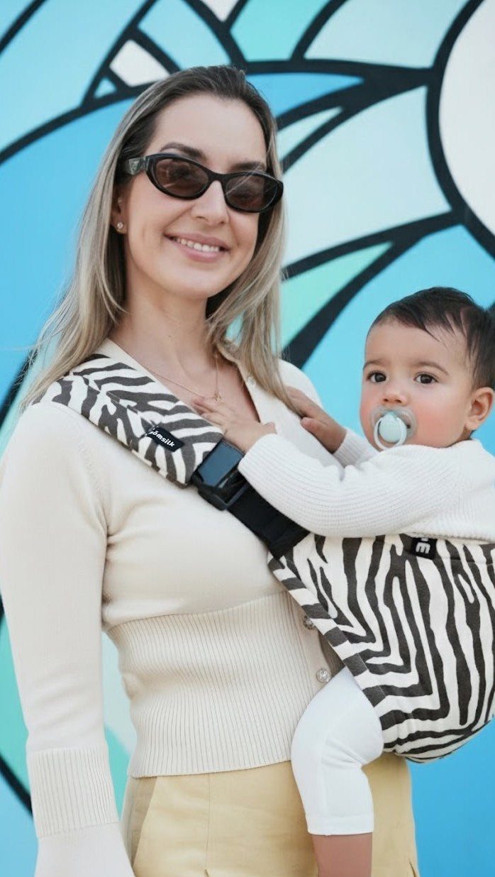 Woman wearing a zebra-print baby carrier with a baby inside against blue background.
