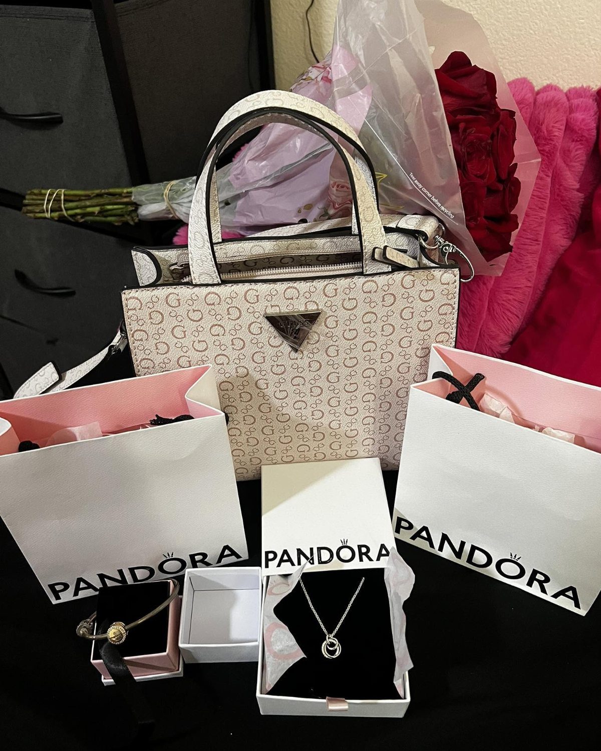 White patterned handbag, Pandora jewelry boxes, and red roses as luxury gifts.
