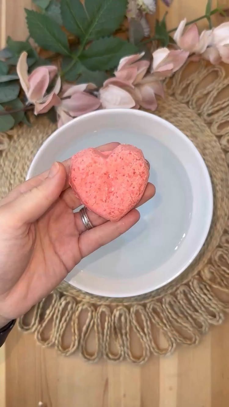 18 Mothers Day Gifts to Make: Easy Handmade Ideas for Mom 14 Pink heart-shaped bath bomb held over a white bowl of water with flowers.
