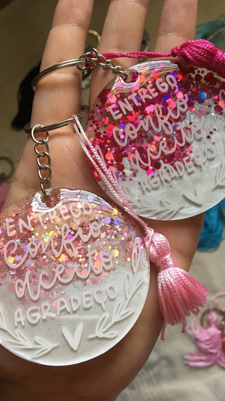 18 Mothers Day Gifts to Make: Easy Handmade Ideas for Mom 12 Two circular resin keychains with pink glitter and Portuguese text held in a hand.