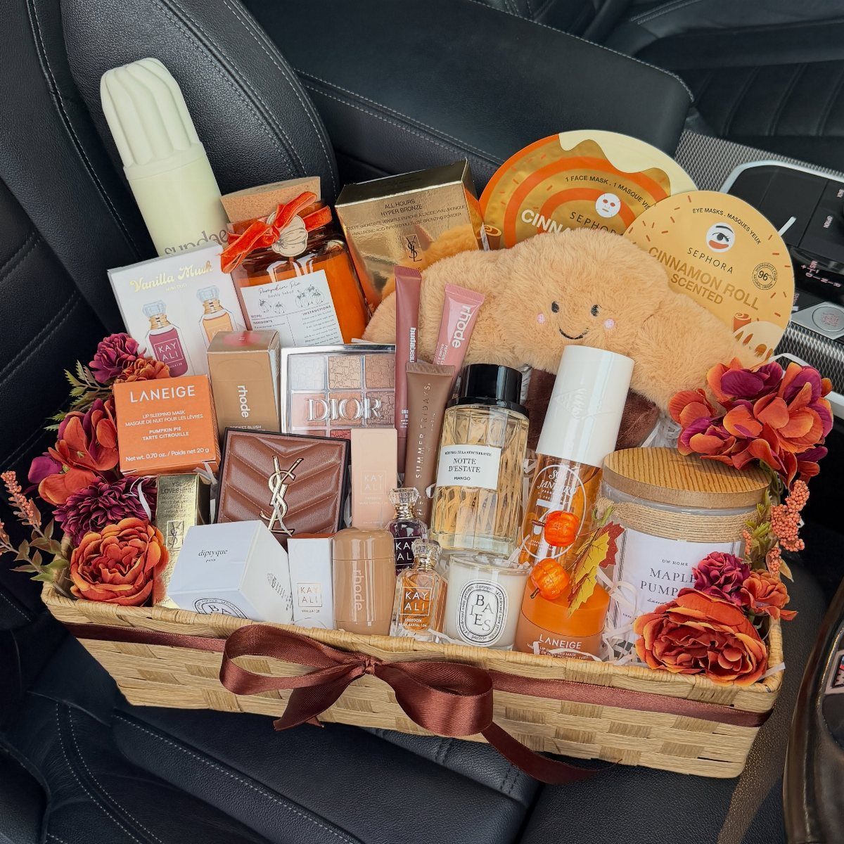 Woven gift basket filled with orange beauty products, skincare, and autumn flowers.