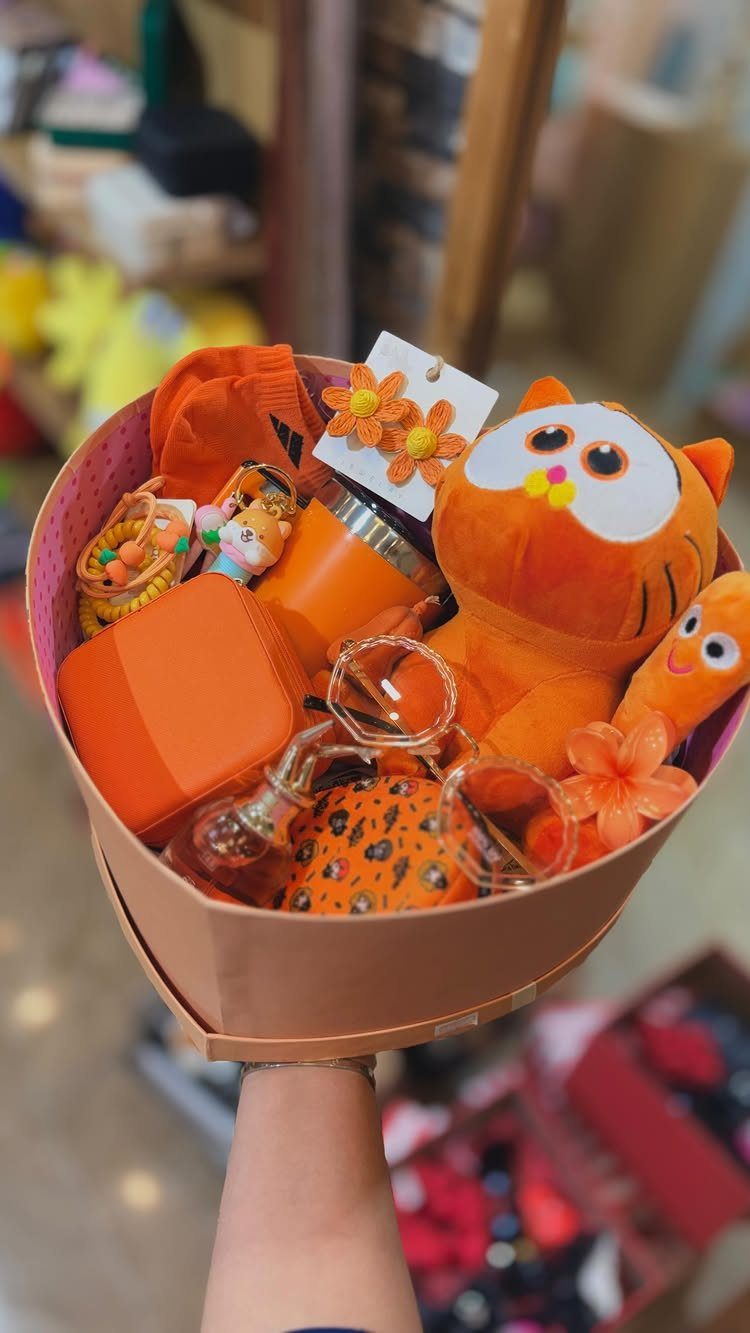 Orange themed gift basket containing a plush cat, socks, and accessories in a box.