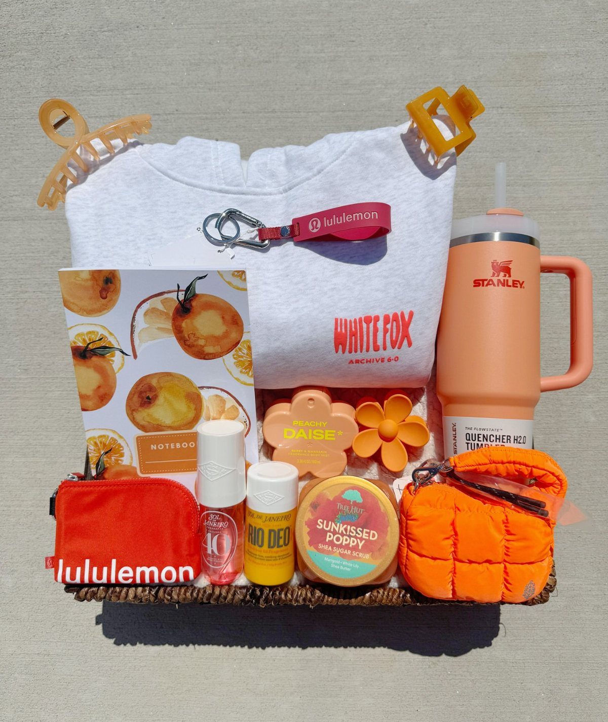 Orange themed gift basket containing a white sweatshirt, orange tumbler, and beauty products.