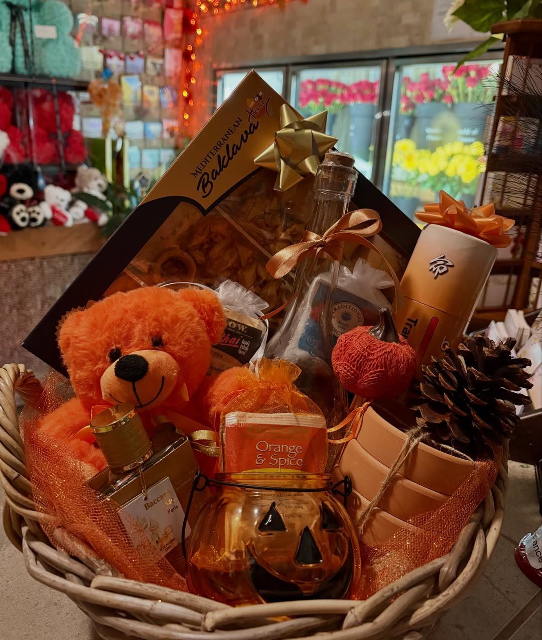 Wicker gift basket containing an orange teddy bear, pumpkin jar, and autumn treats.