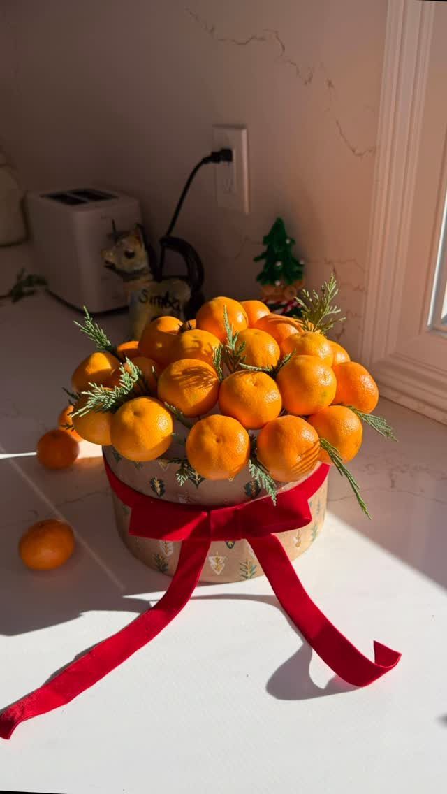 Tangerines and green sprigs in a round gift box tied with red ribbon