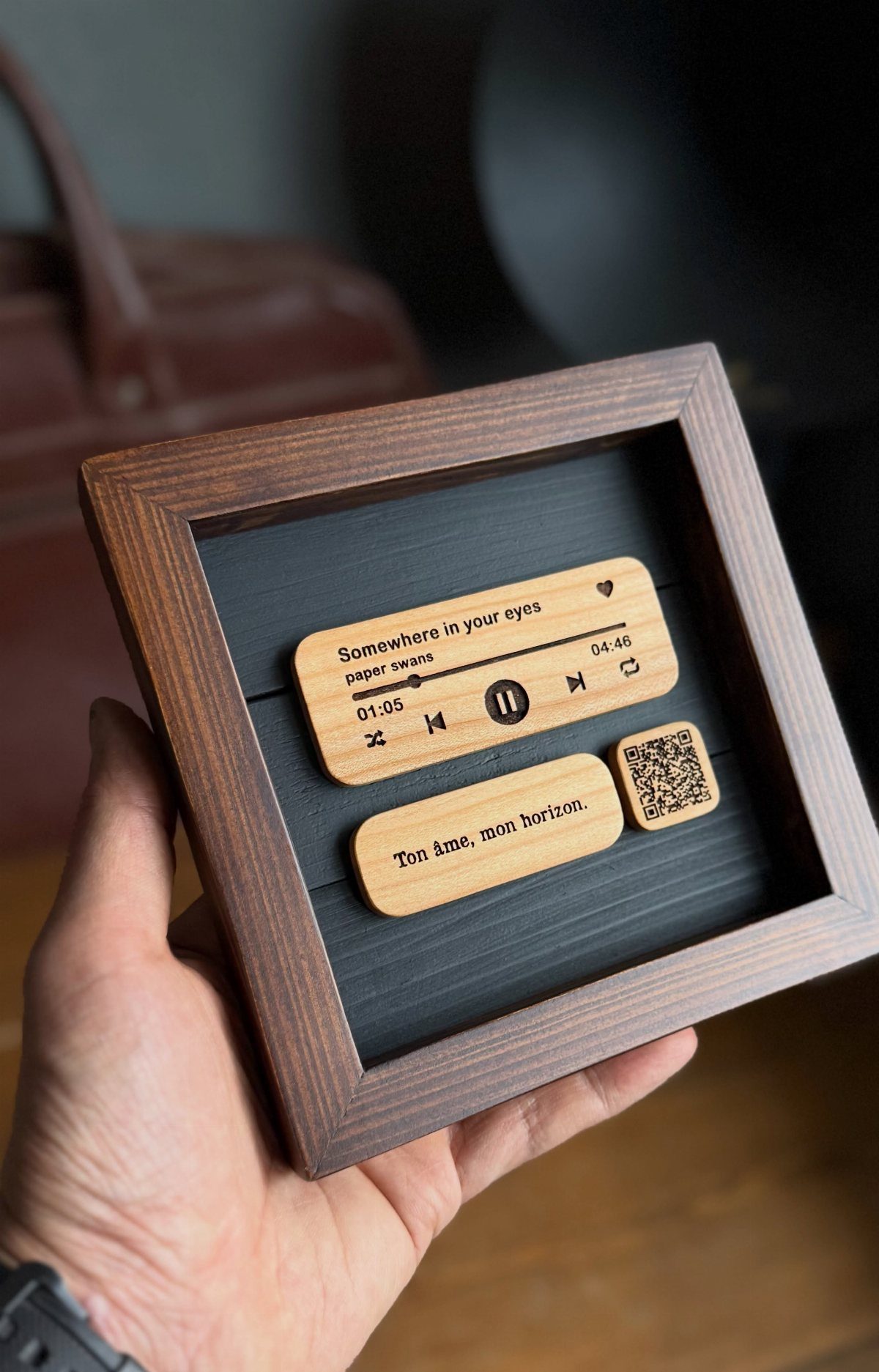 Wooden music player plaque in a frame held by a person's hand.