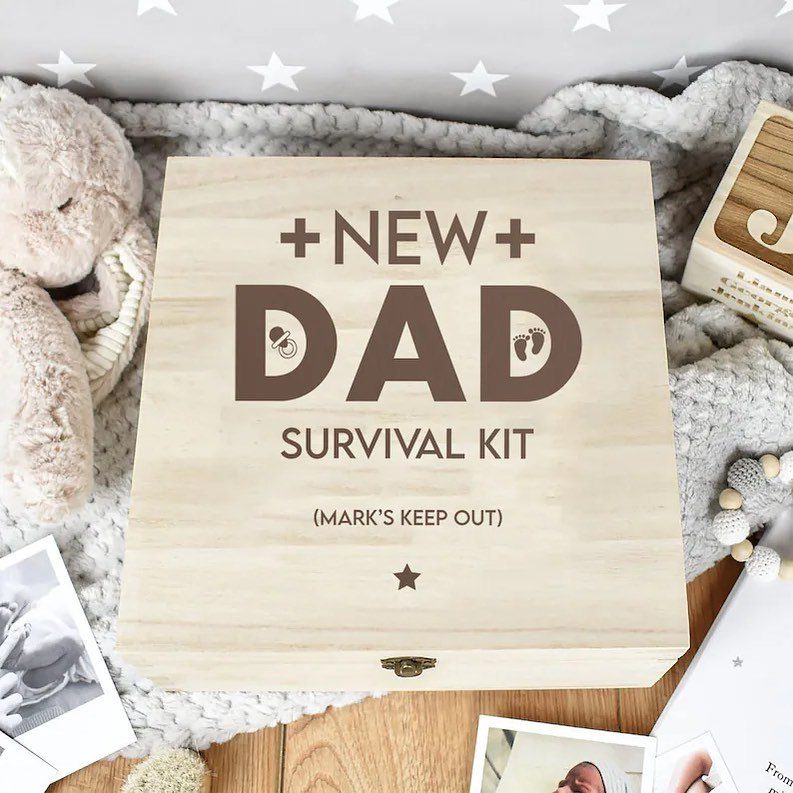 Wooden New Dad Survival Kit box on a white blanket with baby accessories