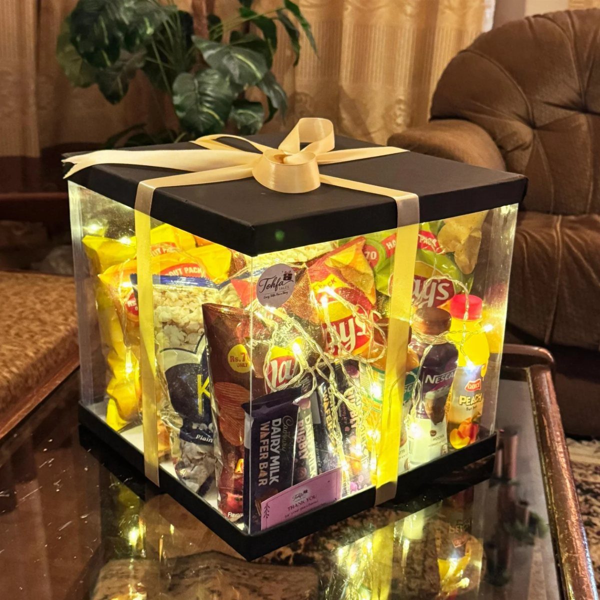 17 Personalized Gifts for Friends: Ideas for Every Budget 1 Clear acrylic gift box filled with assorted snacks and illuminated by fairy lights.