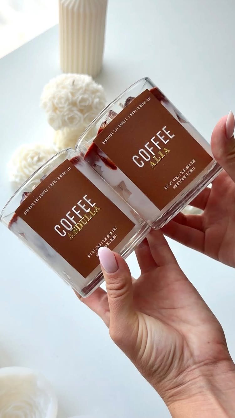 17 Personalized Gifts for Friends: Ideas for Every Budget 7 Two personalized coffee-themed candles in glass jars held by a person's hands.