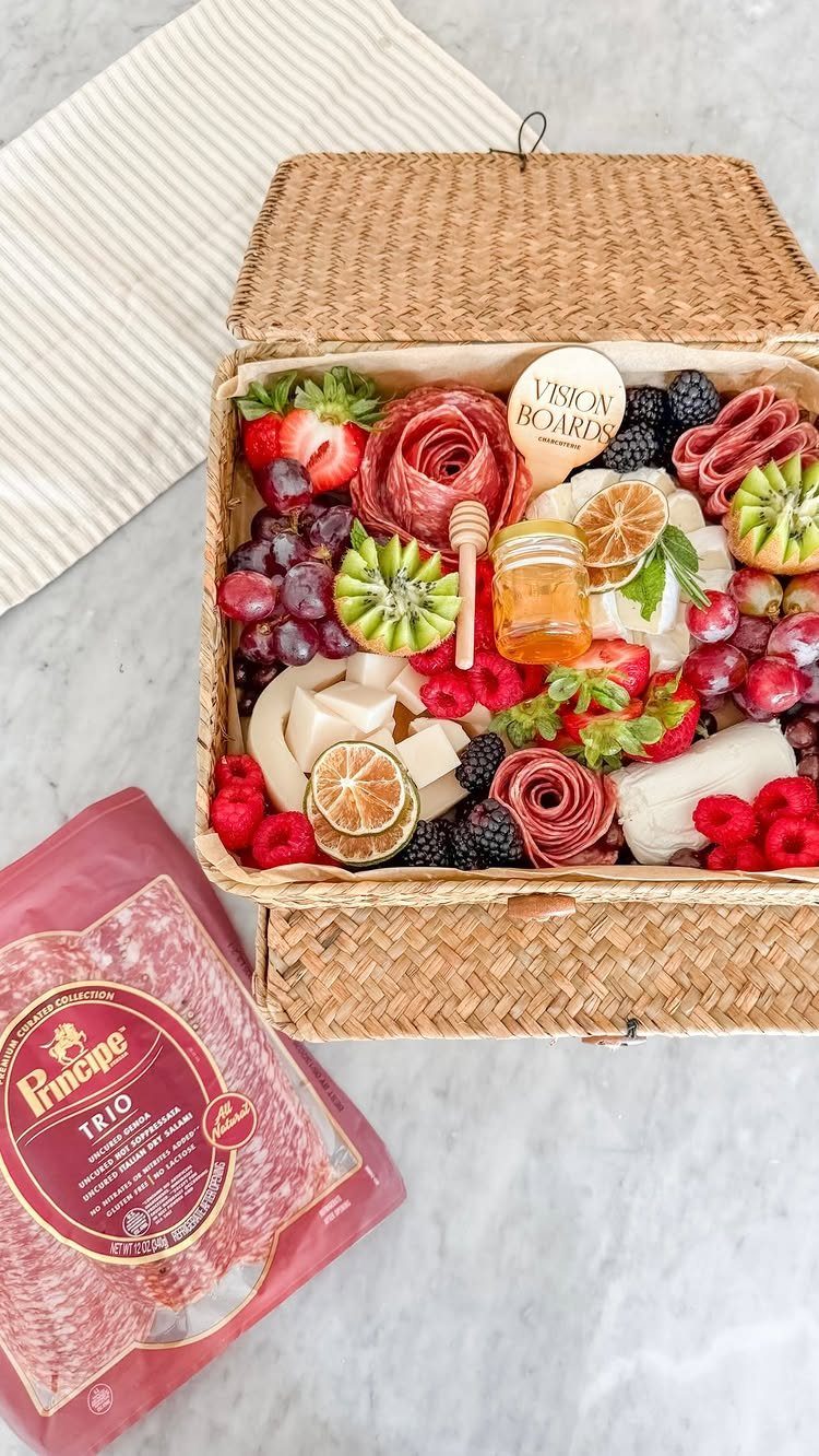 Woven picnic basket filled with fresh fruits, cheeses, cured meats, and honey.