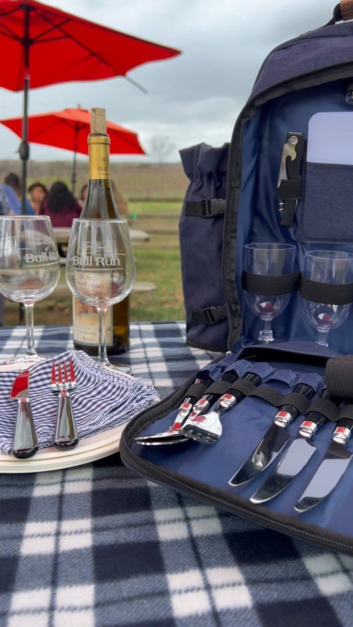 Navy blue picnic backpack with cutlery and wine glasses on a checkered blanket.