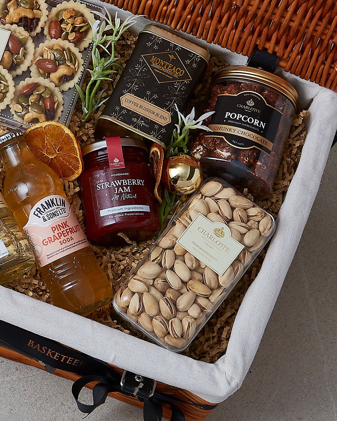 Gourmet picnic basket gift filled with soda, jam, nuts, and sweet treats.