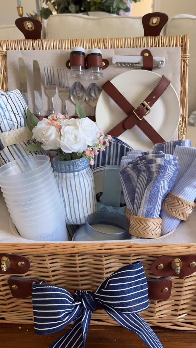 Woven picnic basket gift set with striped napkins, white roses, and dining accessories.