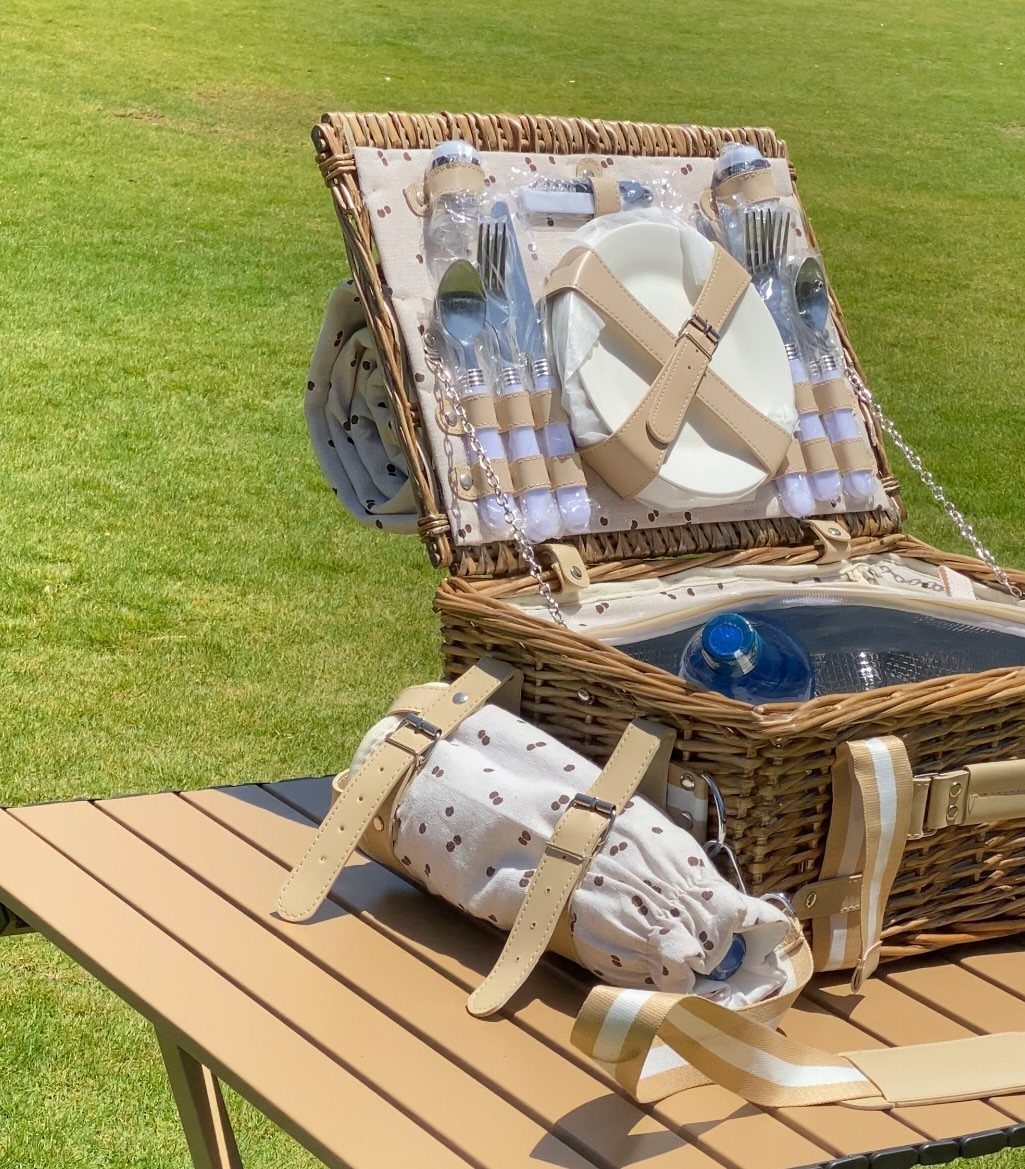 Wicker picnic basket open on a wooden table with plates and cutlery inside.