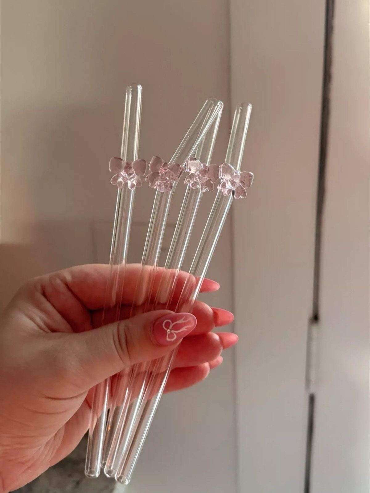 24 Pink Christmas Gift Ideas from Cozy to Glam 22 Clear glass straws with pink bows held by a hand with pink nails.