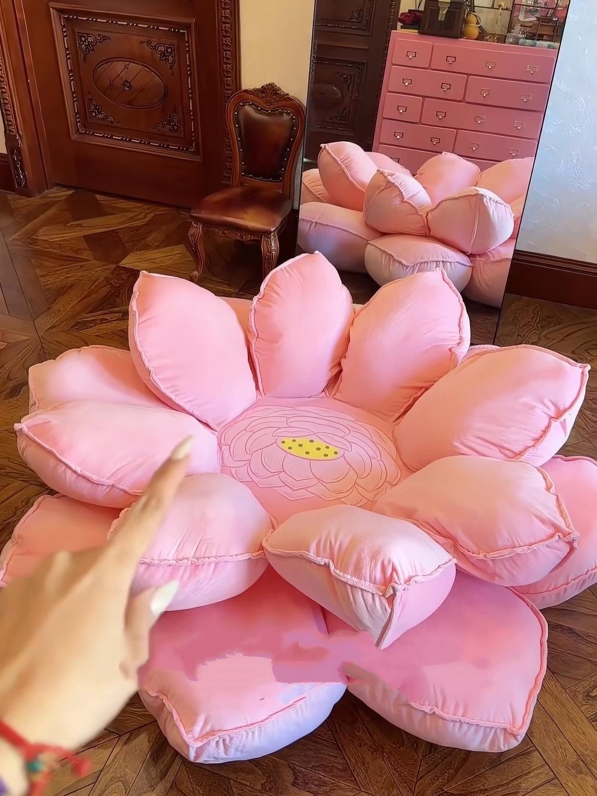 24 Pink Christmas Gift Ideas from Cozy to Glam 8 Pink flower-shaped floor pillow on a wooden floor with a hand pointing to it.