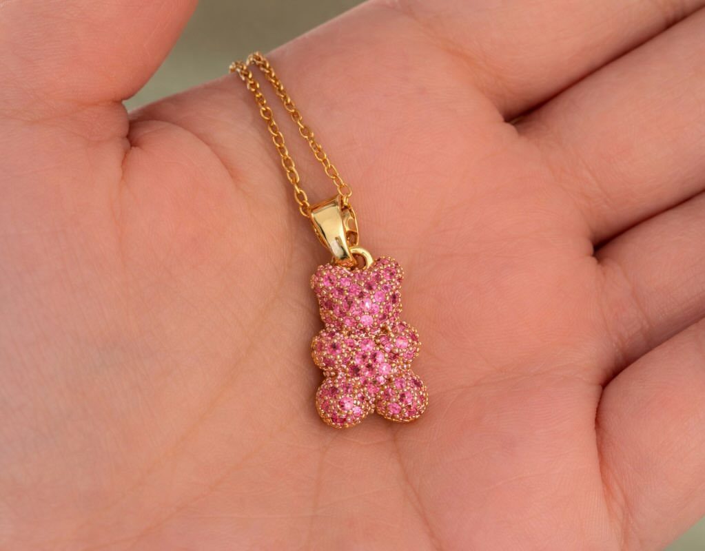 24 Pink Christmas Gift Ideas from Cozy to Glam 23 Gold gummy bear necklace with pink gemstones resting in a person's palm