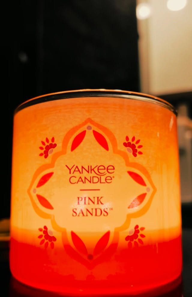 24 Pink Christmas Gift Ideas from Cozy to Glam 3 Pink Sands Yankee Candle jar lit with a glowing orange and pink gradient.