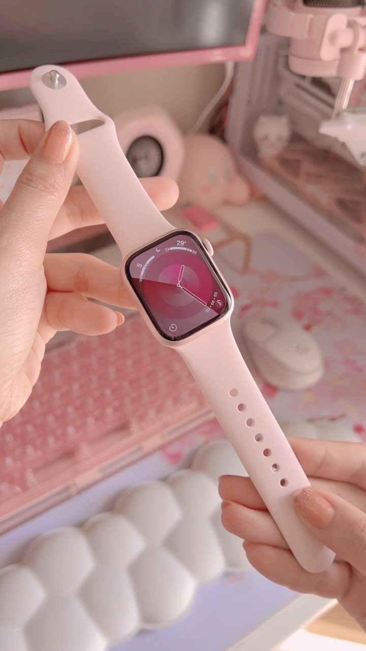 24 Pink Christmas Gift Ideas from Cozy to Glam 13 Pink smartwatch held by hands over a pink and white desk setup.
