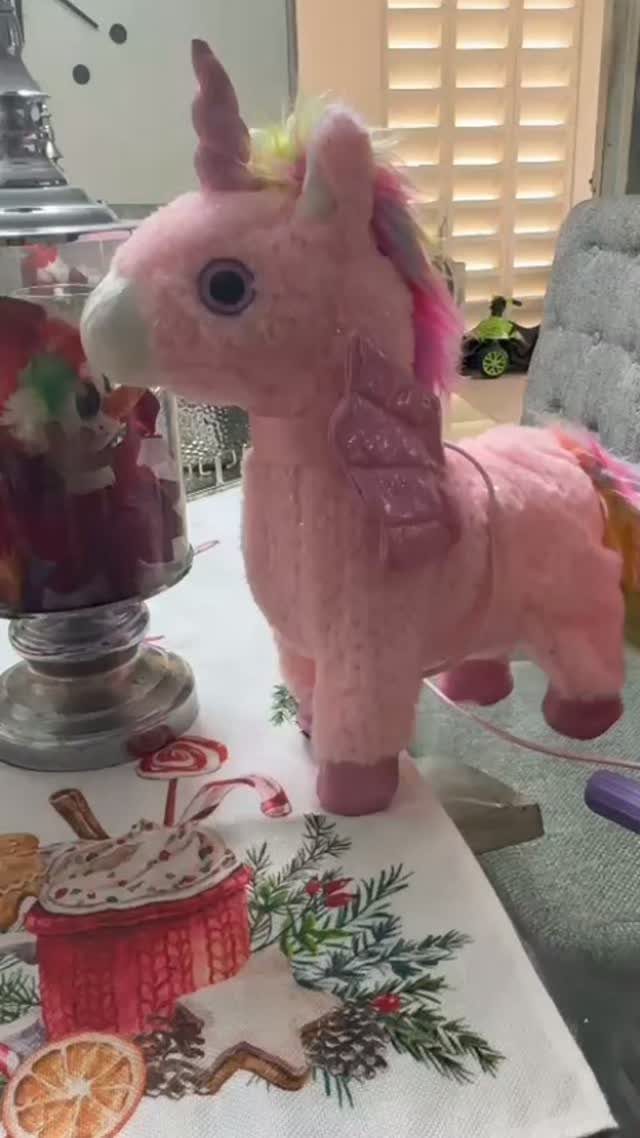 24 Pink Christmas Gift Ideas from Cozy to Glam 24 Pink plush unicorn toy standing on a Christmas themed fabric runner next to candy.