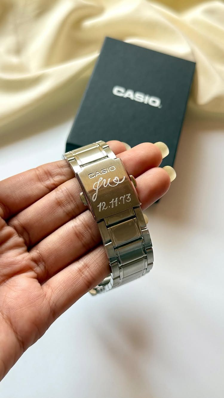 Engraved silver Casio watch held in a hand next to its black box