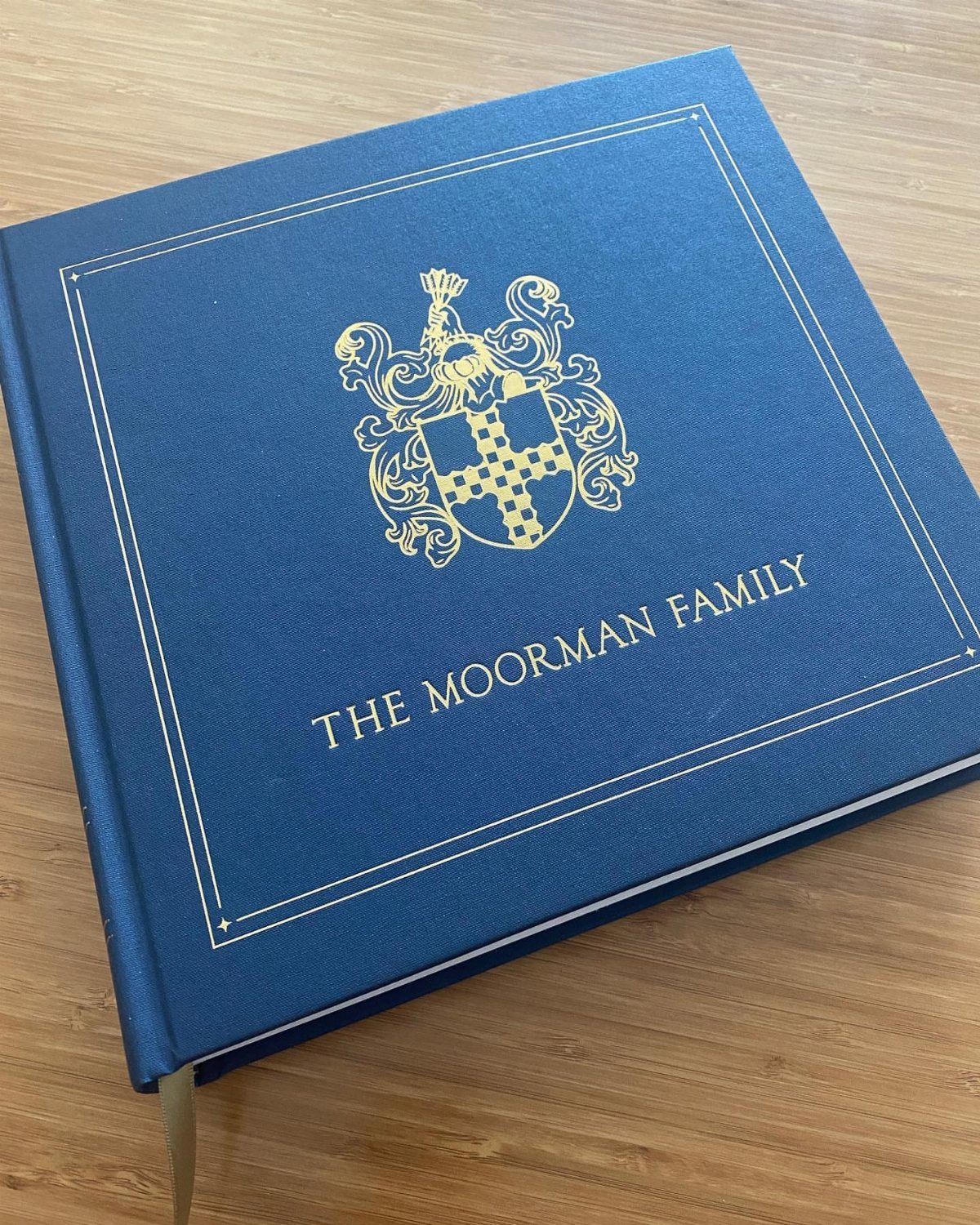 Blue hardcover family history book with gold crest and text on wooden table