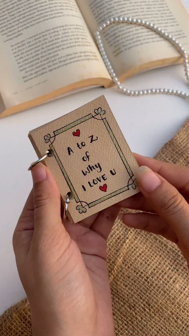 Handmade A to Z love notebook held by hands with a book background