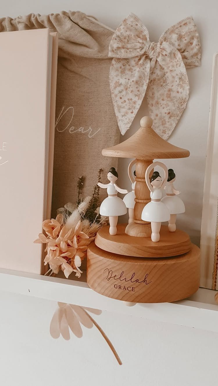 Wooden ballerina music box engraved with a name, surrounded by dried flowers and fabric.