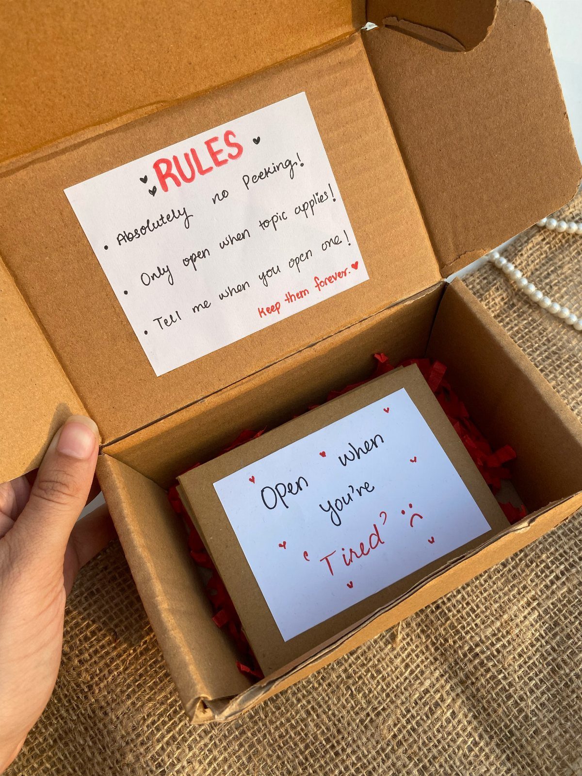 Cardboard gift box with open-when letters and a rules card on burlap fabric