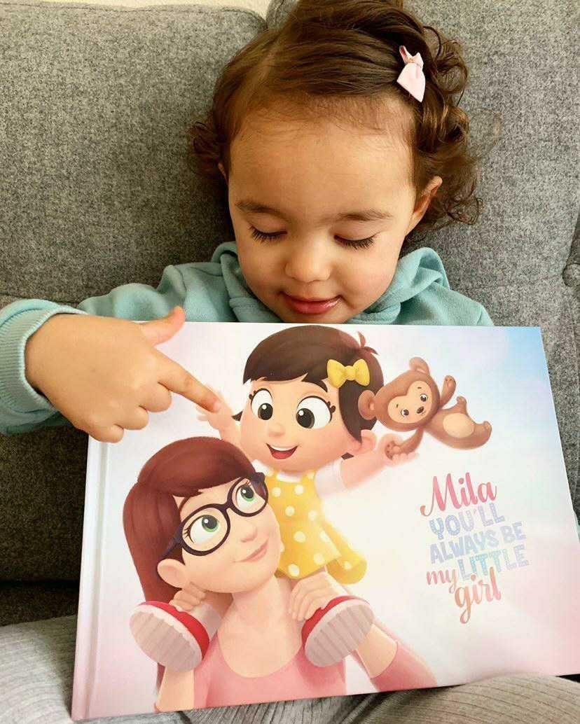 Young girl pointing at a personalized children's book with a cartoon illustration.