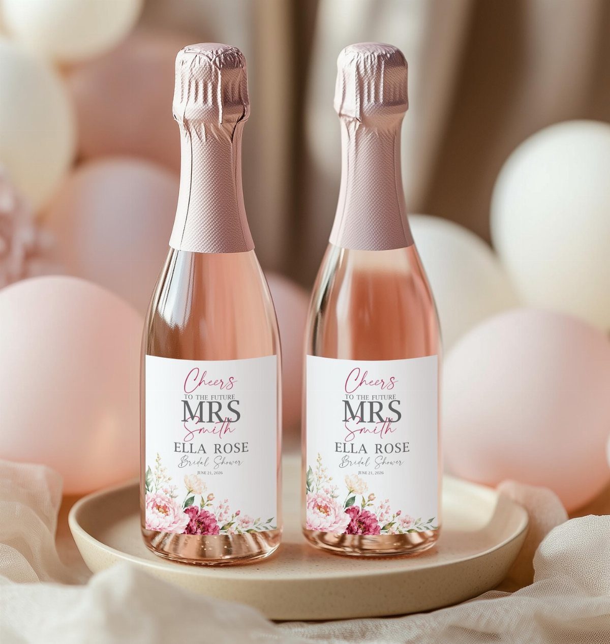 Two pink sparkling wine bottles with personalized floral labels on a beige plate.