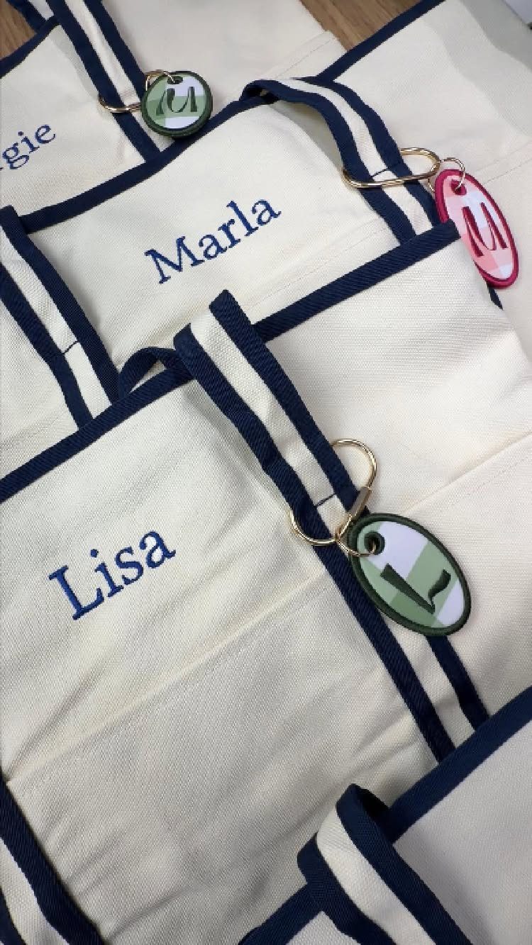 Personalized cream canvas tote bags with navy blue trim and embroidered names.