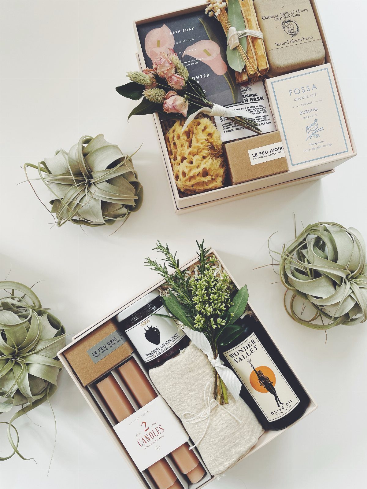 Two curated gift boxes with soaps, candles, and flowers on a white background.