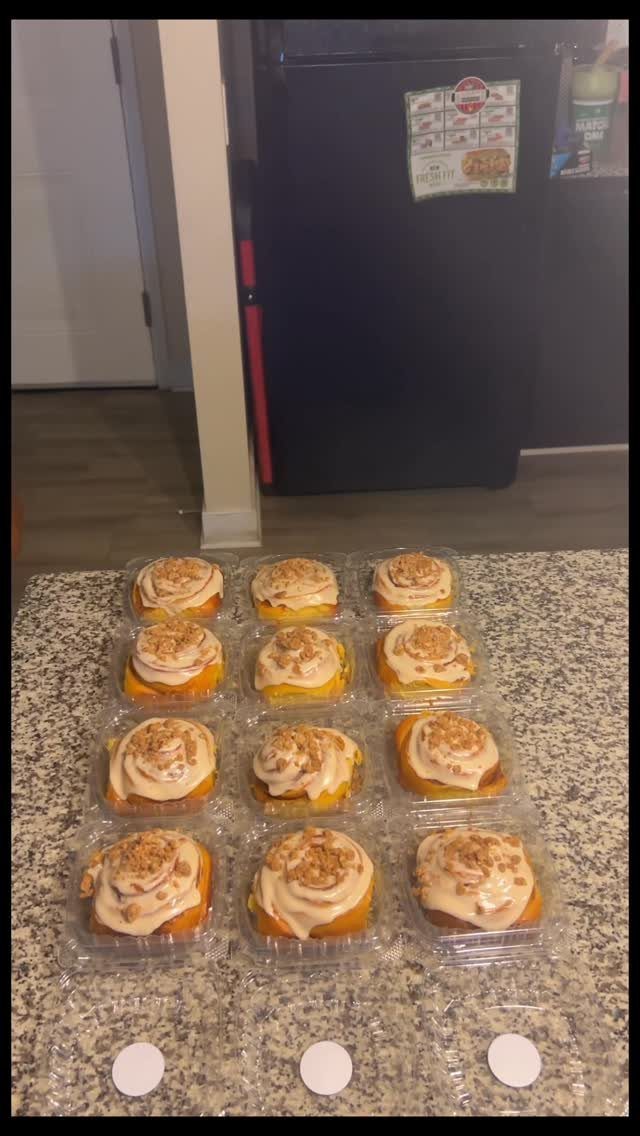 Frosted cinnamon rolls in individual clear plastic containers on a granite countertop.