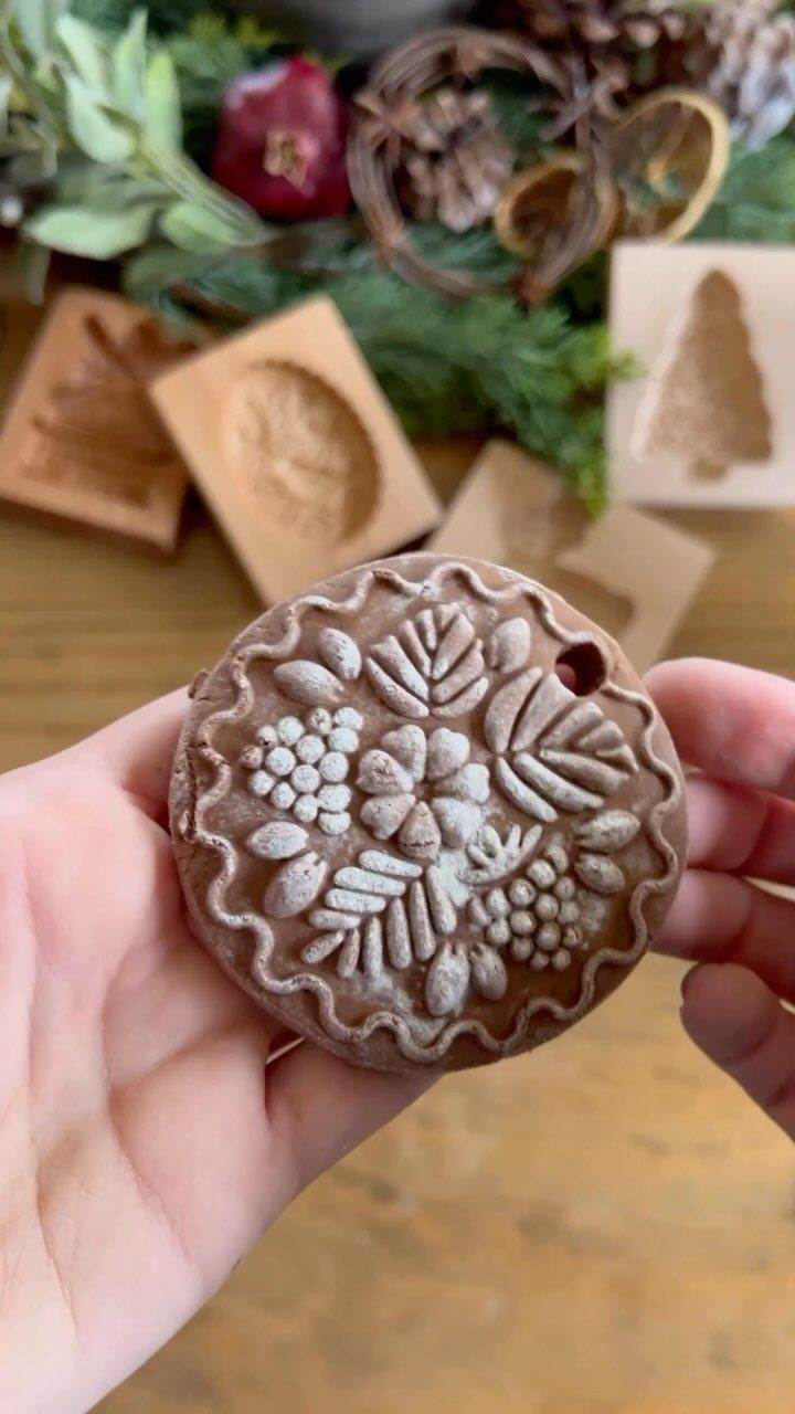 Decorated gingerbread cookie with floral patterns held in hands against festive background