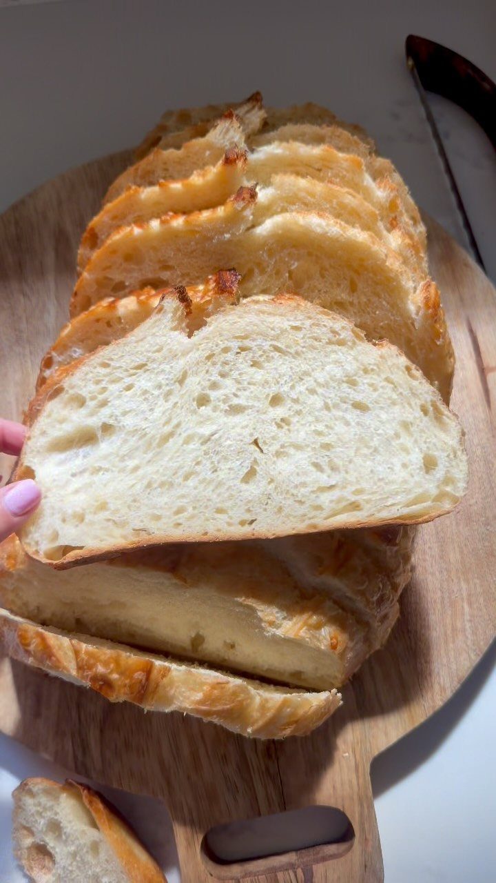 Sliced golden-brown homemade bread loaf on a wooden cutting board with one slice lifted.