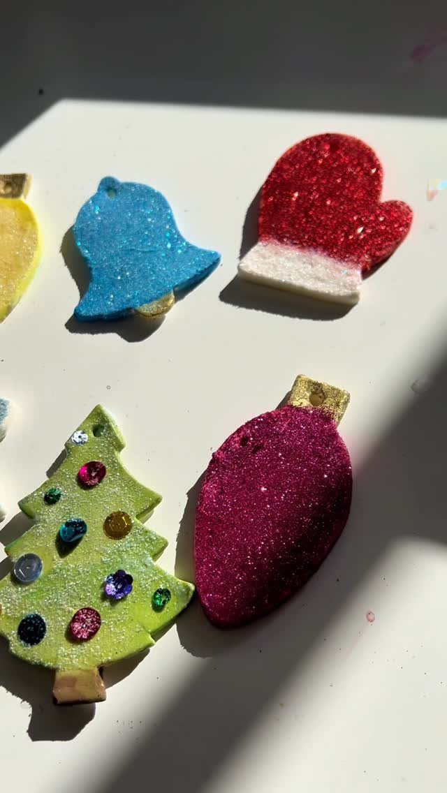 Glittery homemade Christmas ornaments including a tree, mitten, bell, and pink bauble.