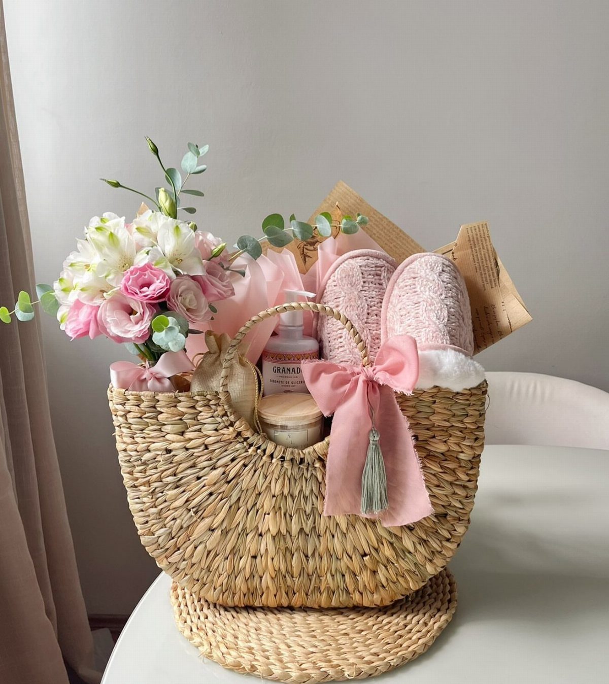 Spa Gift Basket Ideas: 8 Picks for Relaxing at Home 2 Woven straw gift basket containing pink slippers, skincare products, and fresh pink flowers.