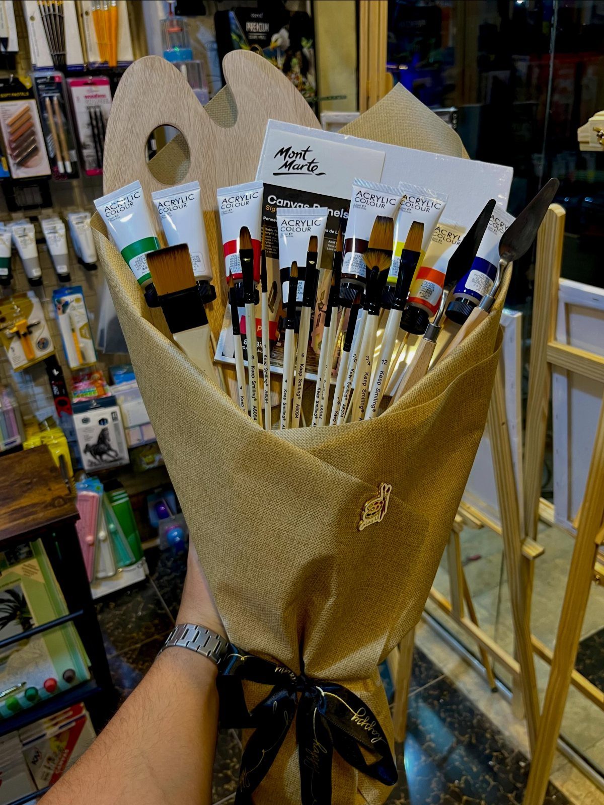 Art supplies bouquet with paintbrushes, acrylic tubes, and a palette wrapped in burlap.