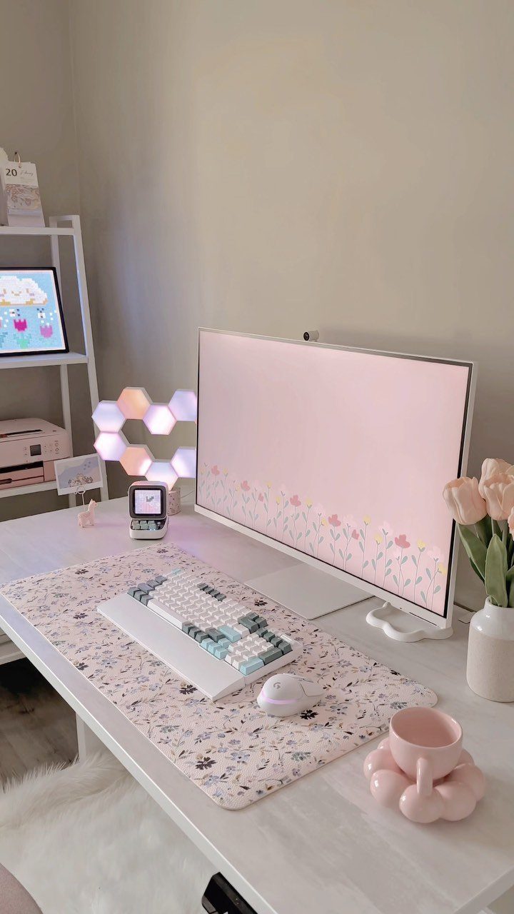 White desk setup with pink floral desk mat, monitor, and pink tulips.